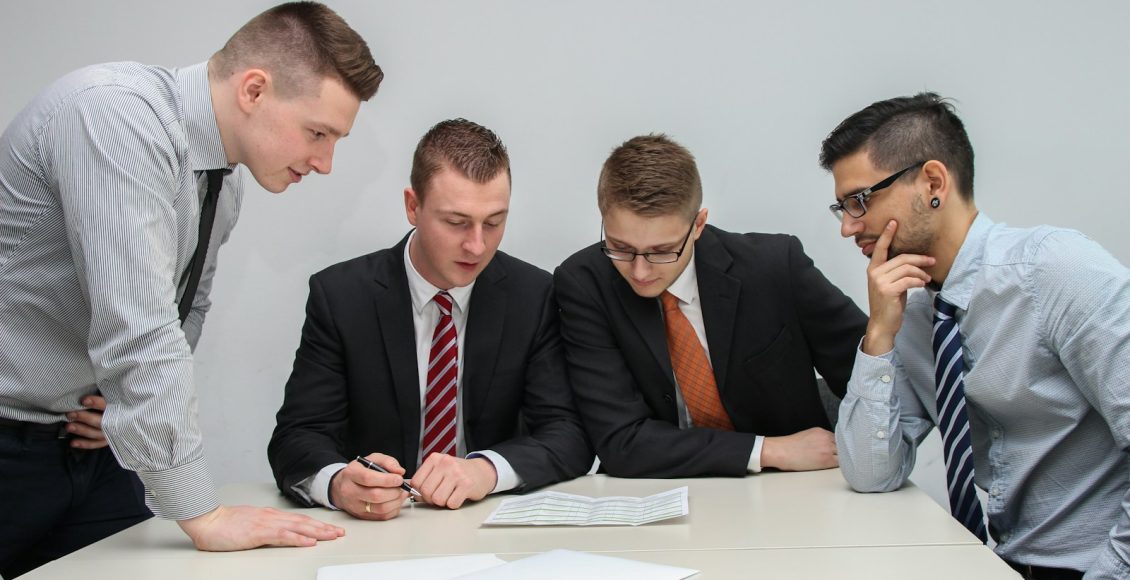 four men looking to the paper on table