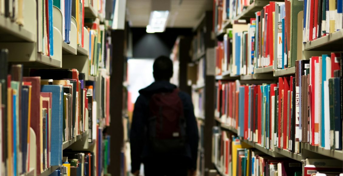 man with backpack beside a books